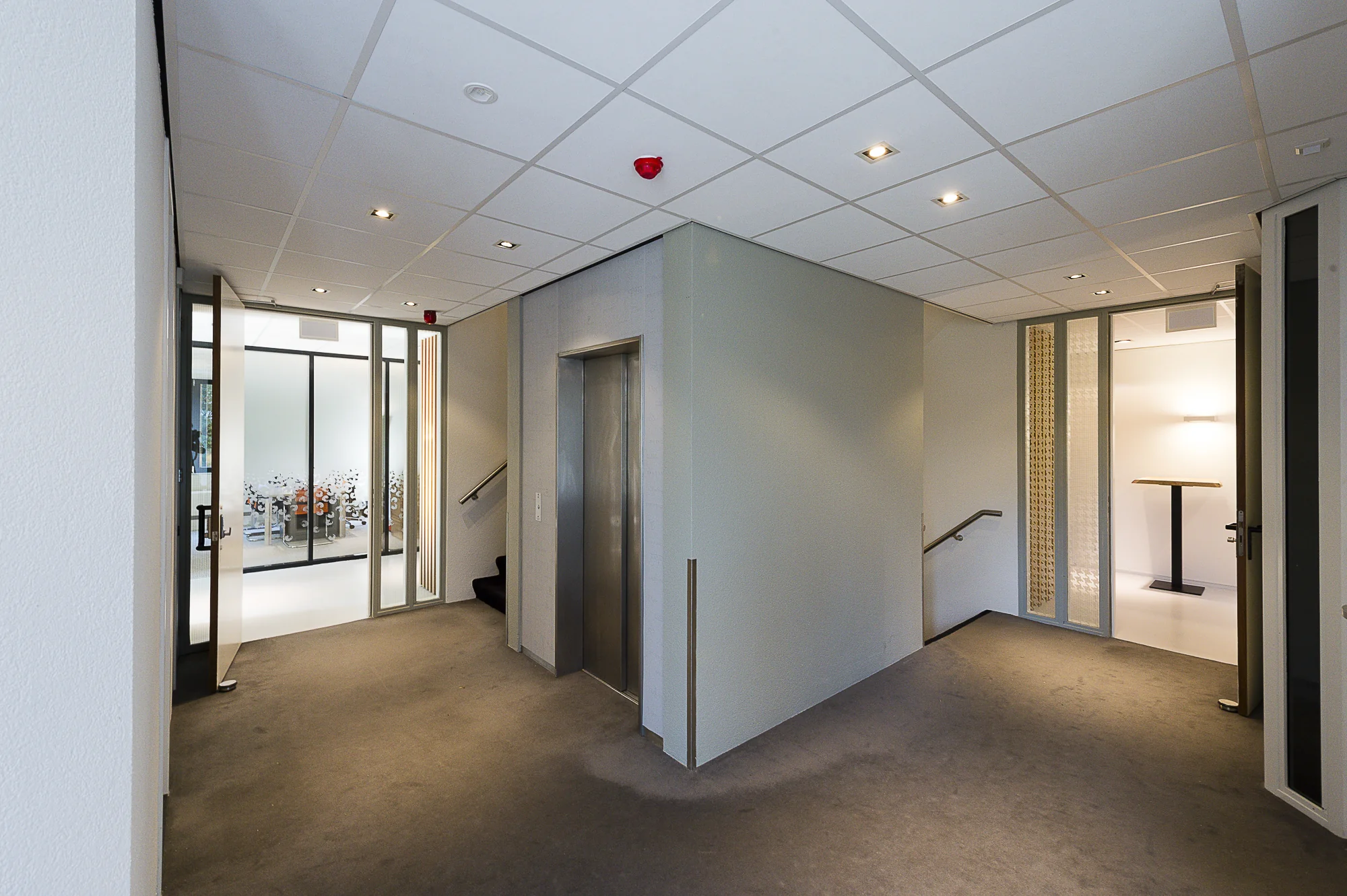 Modern kantoorgebouwinterieur met lift, trap en glazen deuren aan de Max Euwelaan.